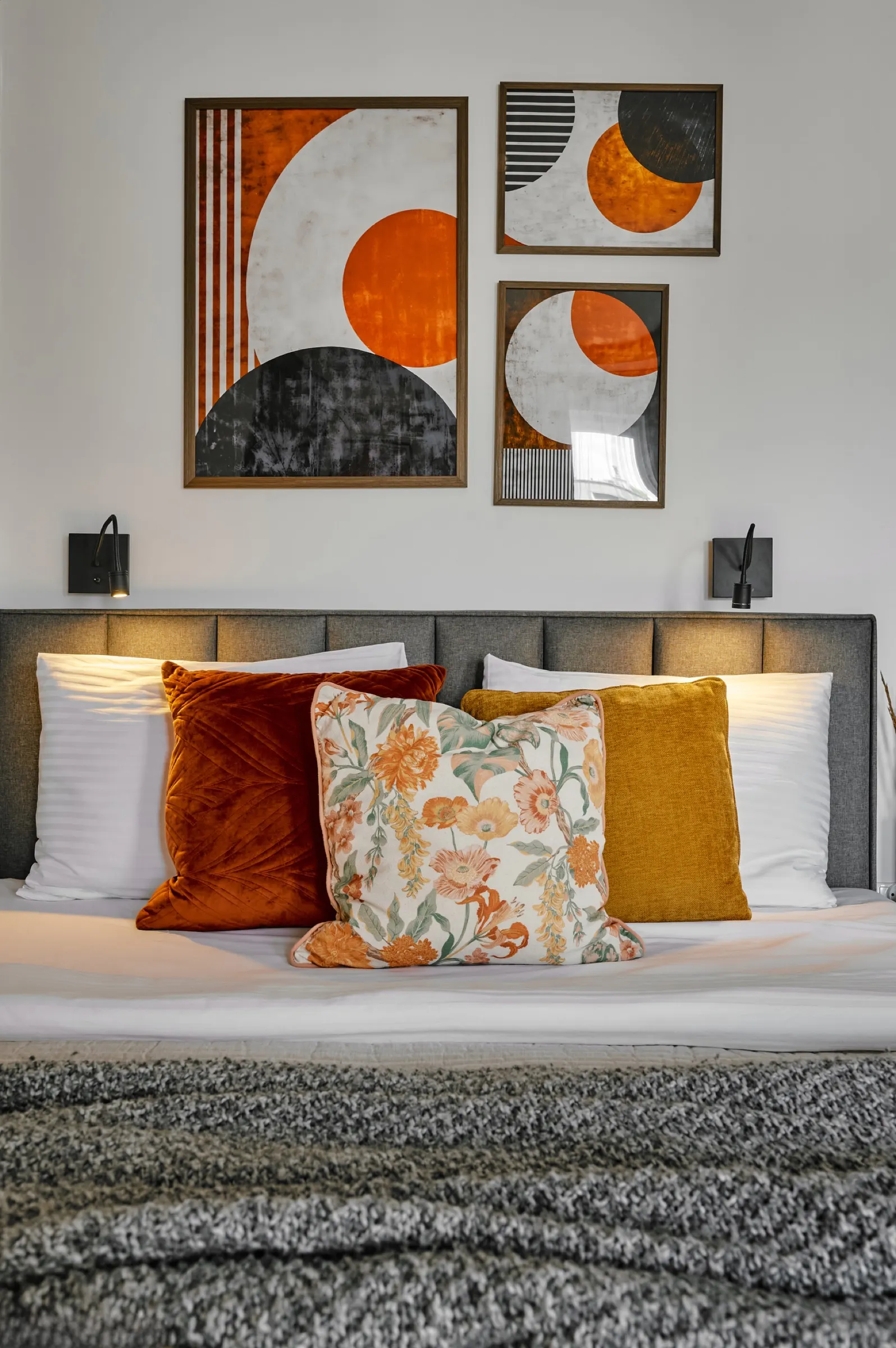 Bed with orange cushions and prints above the headboard