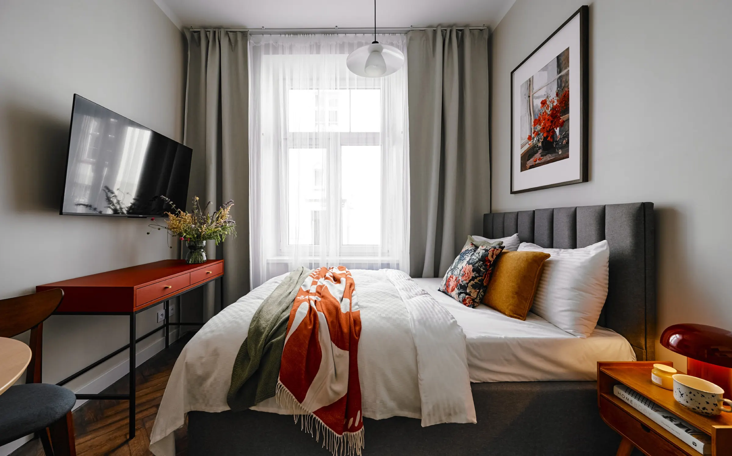 Studio with the bed, a red desk and a curtained window