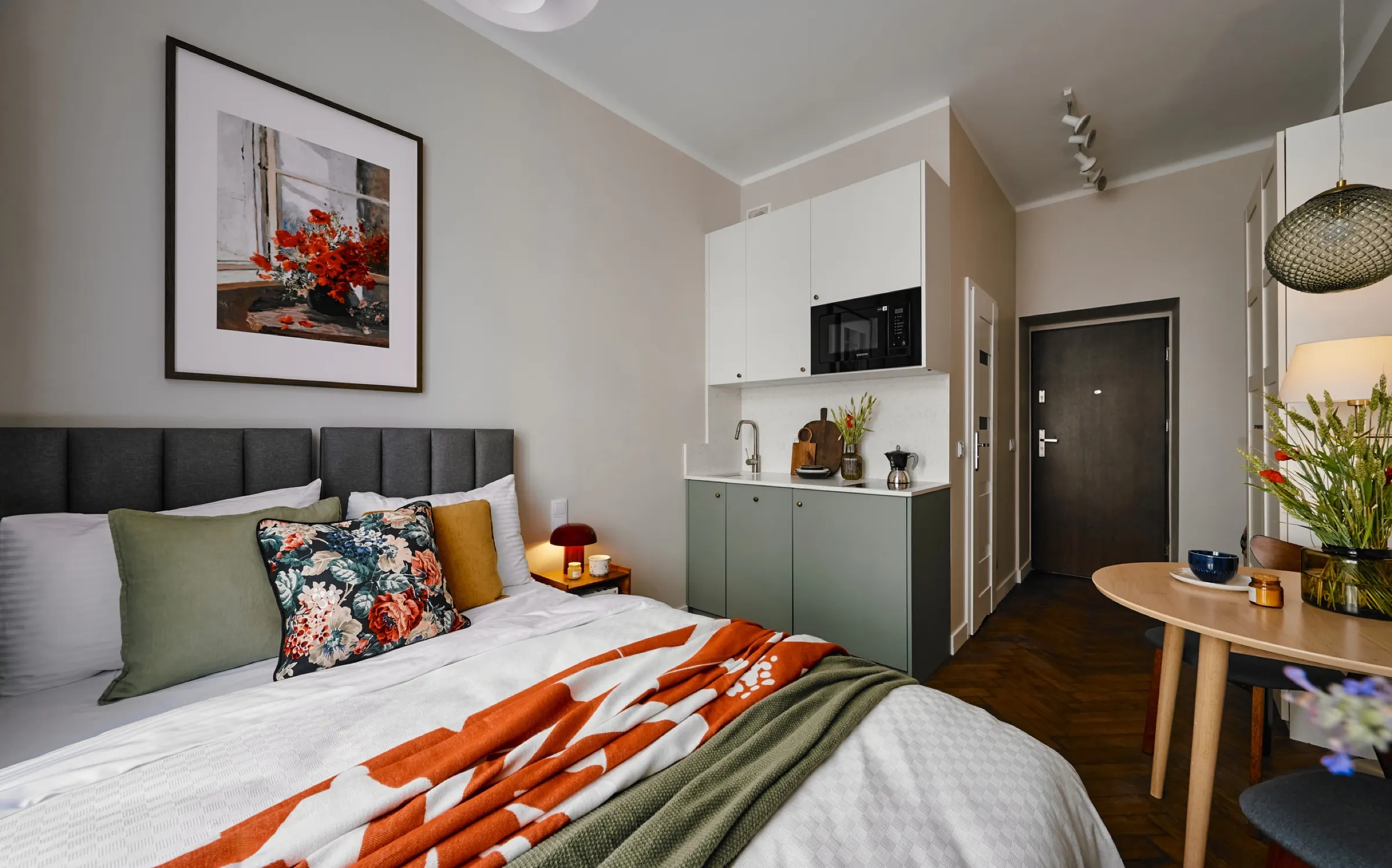 Bed with a colourful throw and the kitchenette behind